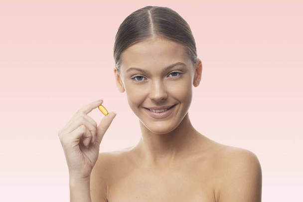 Young woman is holding evening primrose oil capsule. - Фото, зображення