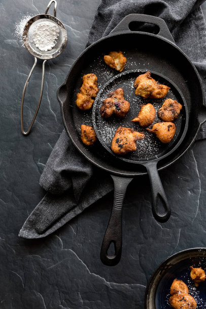 A display of black frypans with homemade fruit filled fritters and icing sugar sprinkled on top. - Foto, immagini