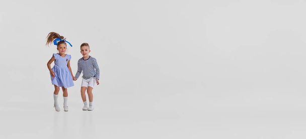 Playful little children in casual stylish clothes having fun together, running isolated over grey background. Flyer. Concept of childhood, creativity, retro style, vintage fashion, friendship, art - Fotoğraf, Görsel
