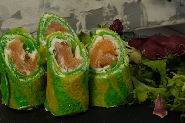 Green pancakes, New Year's bright snack, folded dough rolls, serving pancakes for Shrovetide. Filled with salmon and tender cheese. Zebra dough. Unusual serving food. Cooking, delicious food - Photo, Image