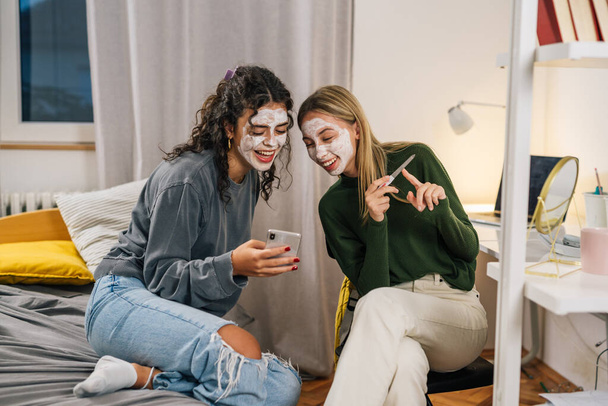 amies avec masque de crème cosmétique sur le visage profiter du temps ensemble dans la chambre - Photo, image