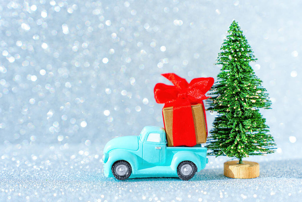 Vintage blue pickup truck with a large christmas present package parked by a toy new year tree against a glittering background imitating snowing. - Foto, afbeelding