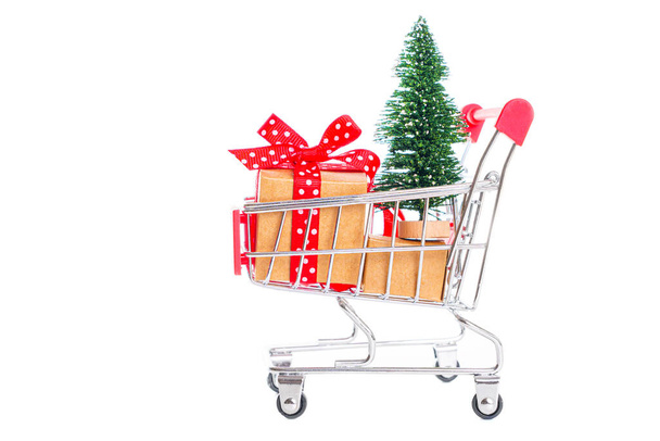 Albero di Natale giocattolo e regali avvolti in un carrello della spesa in miniatura isolato su bianco. Prepararsi per la stagione delle vacanze. - Foto, immagini