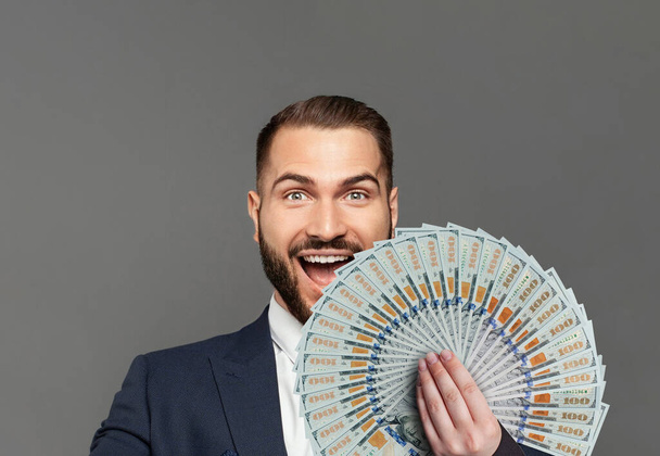 Young happy businessman with really impressive achievements screaming with happiness and fan of money on grey background - Foto, immagini
