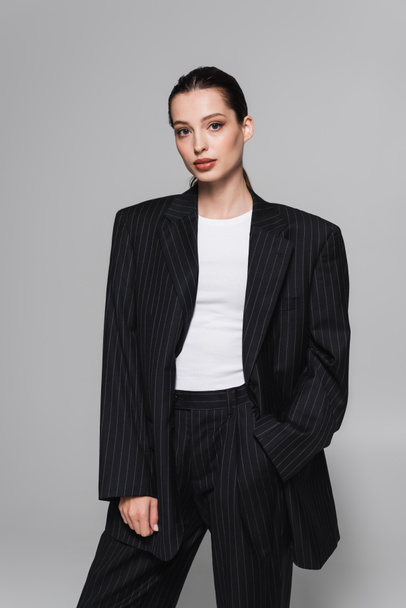 Trendy young woman in black suit posing with hand in pocket isolated on grey  - Foto, afbeelding