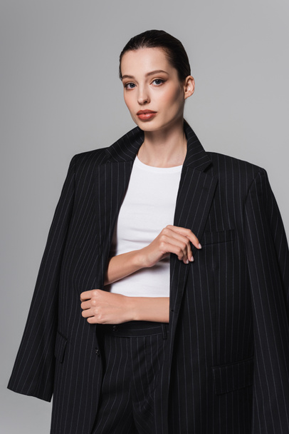 Portrait of stylish brunette model wearing jacket isolated on grey  - 写真・画像