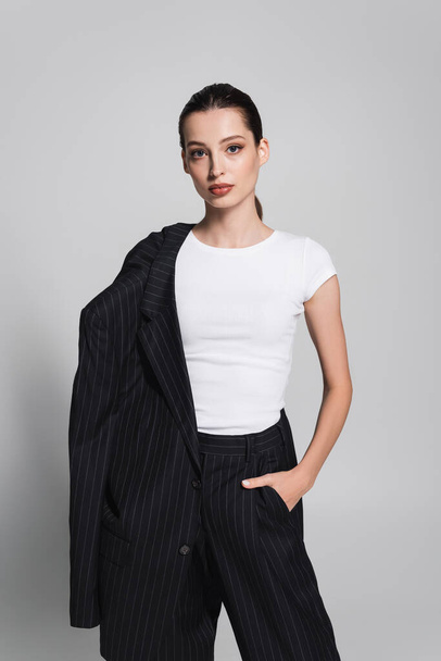 Stylish woman in t-shirt and striped suit posing on grey background  - Foto, Bild