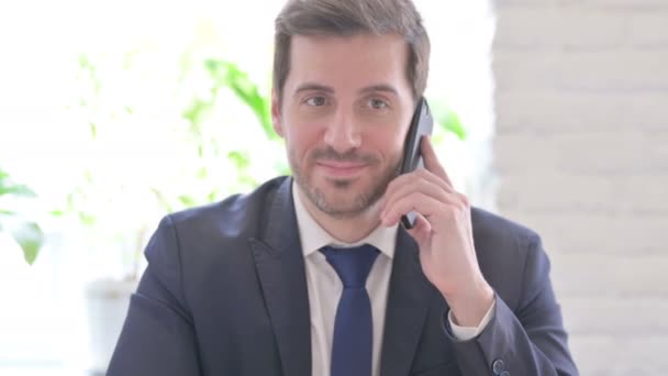 Mladý dospělý podnikatel mluví po telefonu, zatímco v kanceláři - Záběry, video