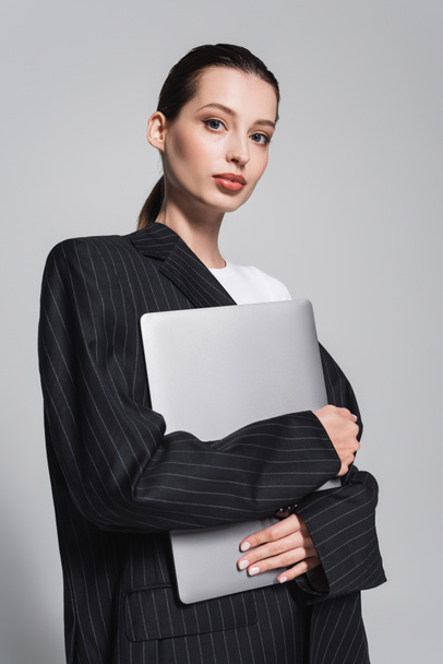 Портрет молодої жінки в смугастій куртці, що тримає ноутбук ізольовано на сірому
  - Фото, зображення