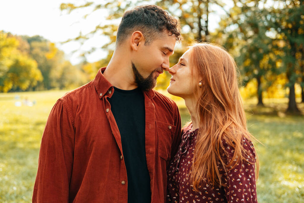 Hűvös fiatal pár szerelmes egymásba megérintik az orrát és mosolyognak. Szabadtéri fotó egy zöld parkban. - Fotó, kép