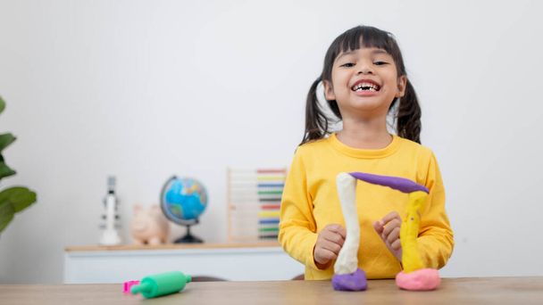 The little girl is learning to use colorful play dough in a room - Photo, Image
