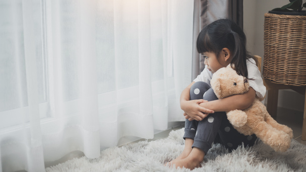 Blisko samotna dziewczynka przytula zabawkę, siedzi sama w domu, zdenerwowane nieszczęśliwe dziecko czeka na rodziców, myśli o problemach, złe relacje w rodzinie, uraz psychiczny - Zdjęcie, obraz