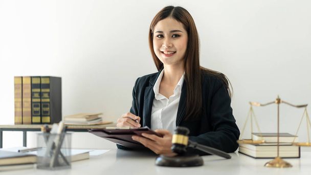 ビジネス弁護士の女性は、法律事務所で真鍮スケールと司法ハンマーでテーブルの上で作業しながら、ビジネス契約を読み、文書にデータを書いています. - 写真・画像