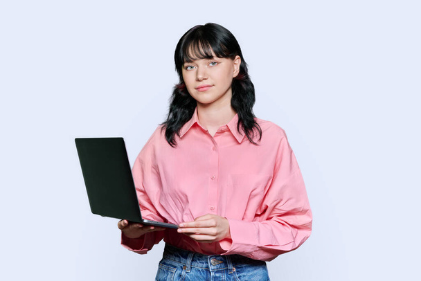 Smiling teenage female student using laptop, girl looking at camera on light studio background. Remote college education e-learning banking, online shopping, lifestyle leisure study technology concept - Фото, зображення