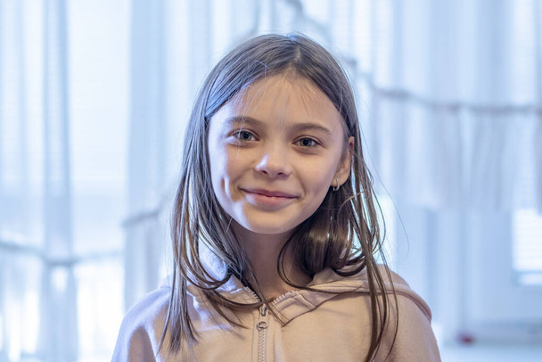 Portret van een 11-jarig meisje tegen de achtergrond van een raam. - Foto, afbeelding