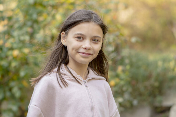 A 10-12-year-old girl with long hair in pink pajamas on a blurry background of nature. - Photo, Image