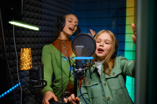 Szczęśliwe dziewczyny w słuchawkach śpiewające w studiu nagraniowym. Widok przez okno - Zdjęcie, obraz