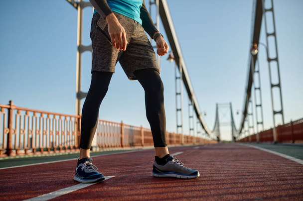 Sport achtergrond met mannelijke loper voeten op brug weg. Close-up sporter jogger been in schoen en sportieve outfit - Foto, afbeelding
