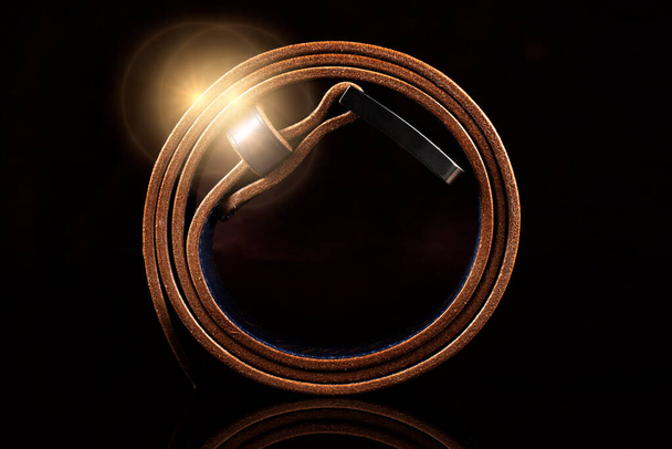 Cinturão marrom de couro em um fundo escuro com reflexão. - Foto, Imagem