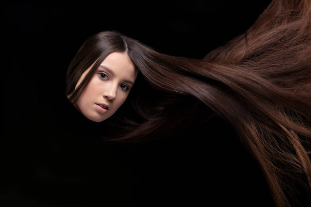 Lange dunkle Haare. Das Gesicht eines Mädchens mit wallenden Haaren auf dunklem Hintergrund. - Foto, Bild