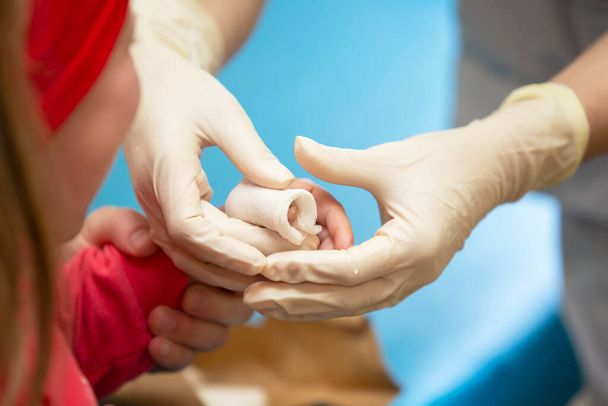 De handen van de arts verbinden de pijnlijke vinger met een verband van het kind. Letsel en wond aan de vinger bij kinderen - Foto, afbeelding
