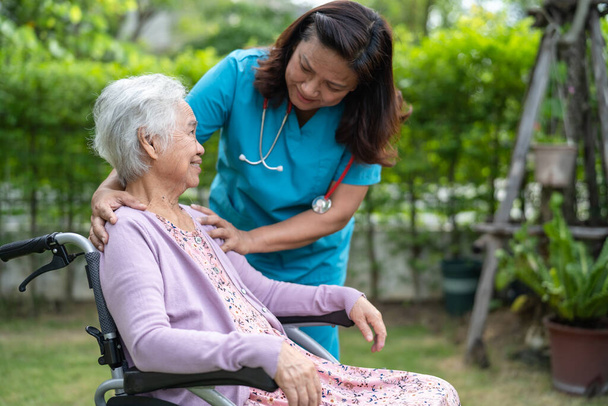 Doctor caregiver help and care Asian senior or elderly old lady woman patient sitting on wheelchair in park at nursing hospital, healthy strong medical concept - Photo, Image