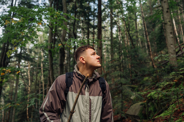 Portrait of a male tourist in casual clothes walking through the forest in the mountains on a hike and looking to the side with a serious face - 写真・画像
