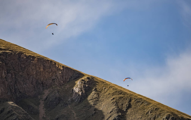 Dwóch spadochroniarzy na paralotni przelatuje nad zboczem góry o błękitne niebo, jesienią w górach - Zdjęcie, obraz