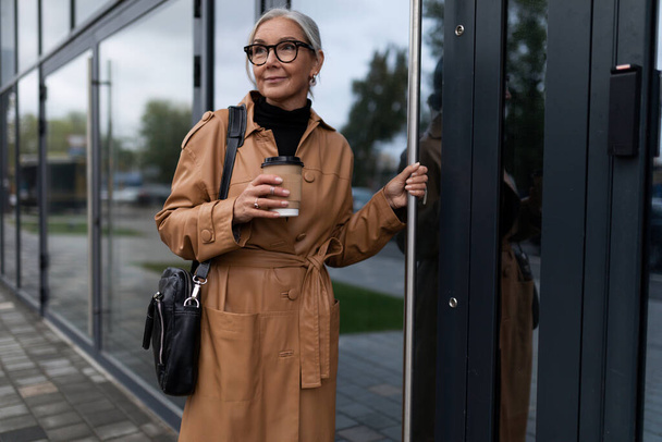 elegante kaukasische Frau mit einer Tasse Kaffee betritt das Bürogebäude. - Foto, Bild