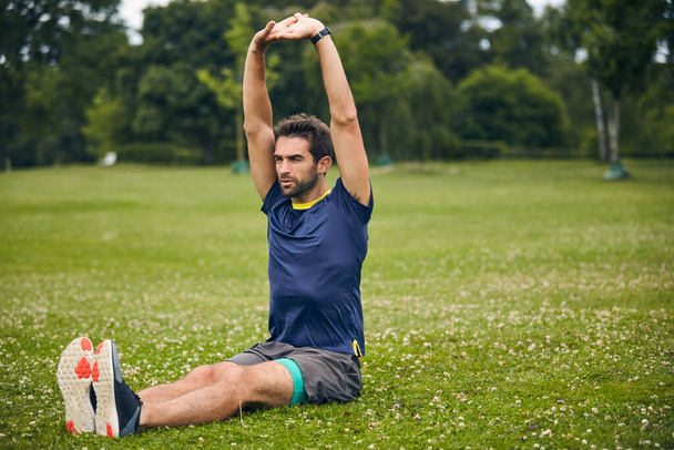Hoe meer je rekt, hoe beter je je zult voelen. een sportieve man begint zijn oefening routine met stretching oefeningen - Foto, afbeelding