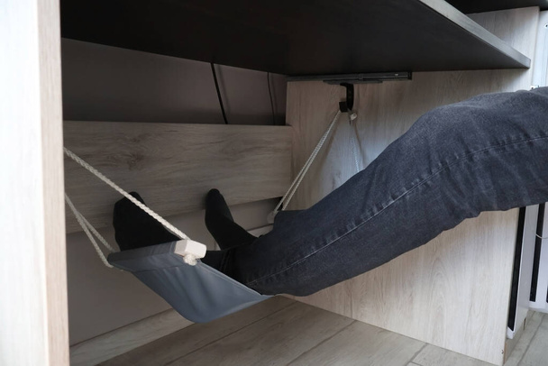 Ноги чоловіка лежать у гамаку під столом. Догляд за здоров'ям вен при варикозі
 - Фото, зображення