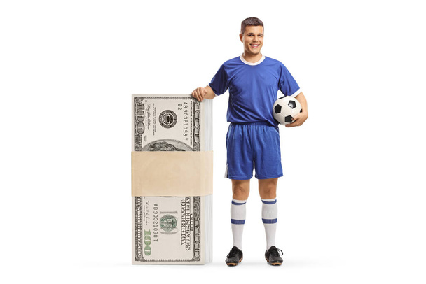 Man in a football jersey standing next to a big stack of money isolated on white background - Zdjęcie, obraz