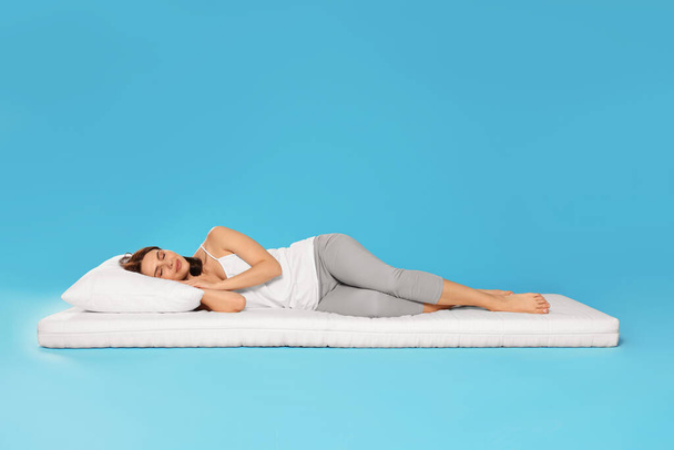 Young woman sleeping on soft mattress against light blue background - Photo, Image