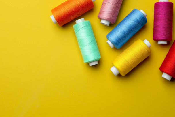 Different colorful sewing threads on yellow background, flat lay. Space for text - Foto, afbeelding