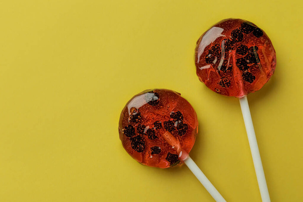 Sweet colorful lollipops with berries on yellow background, flat lay. Space for text - Foto, Imagem