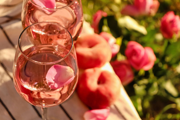 Glasses of delicious rose wine with petals on white picnic blanket outside. Space for text - Foto, Imagem