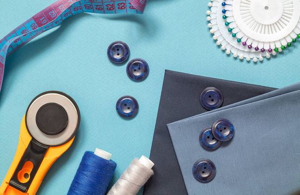 Accessoires naaien voor het afstemmen op een blauwe ondergrond. Roterend mes, stof, knopen, centimeter, pennen, naald, draadspoel. Plat gelegd. Bovenaanzicht. - Foto, afbeelding