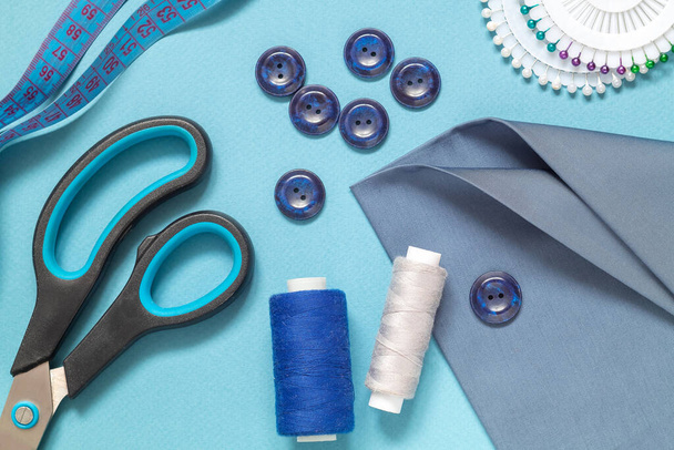 Naaigereedschap voor het naaien op een blauwe ondergrond. Stof, schaar, knopen, centimeter, pennen, naald, draadspoel. Plat gelegd. Bovenaanzicht. - Foto, afbeelding