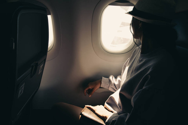 Young traveller woman sitting inside plane on flight watch to sky and plane wing from window - Foto, Imagen