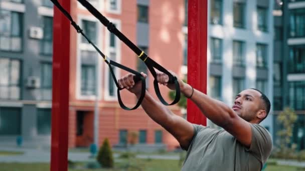 Musclé athlétique puissant latino-américain homme bodybuilder sportif utiliser des équipements de sport en plein air étirement séance d'entraînement sur la ville sports sol suspendus pull ups exercice avec TRX sangles vie saine active - Séquence, vidéo