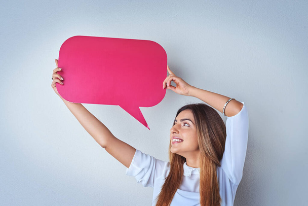 Share your thoughts with the world. an attractive young woman holding up a speech bubble against a blue background - Foto, immagini