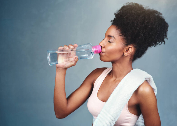 Drinkwater helpt de balans van lichaamsvloeistoffen te behouden. een sportieve jonge vrouw drinken fles water tegen een grijze achtergrond - Foto, afbeelding