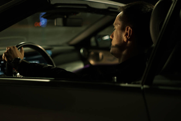 Hombre adulto sentado en un coche por la noche - Foto, Imagen