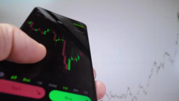 Analista inversor comerciante empresario utilizando la aplicación de teléfono móvil para analizar el mercado financiero criptomoneda, índice gráfico de datos comerciales en el teléfono inteligente. en segundo plano se ejecuta gráfico en pantalla - Metraje, vídeo