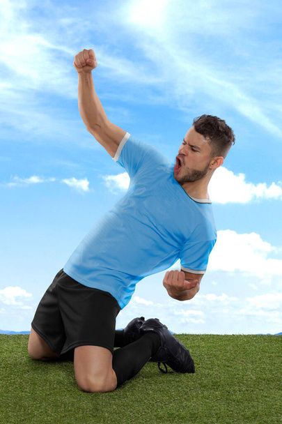 Professionele voetballer met een lichtblauwe Uruguay nationale team trui schreeuwen van opwinding voor het scoren van een doel met een uitdrukking van uitdaging en geluk op het veld gras en wolk achtergrond - Foto, afbeelding