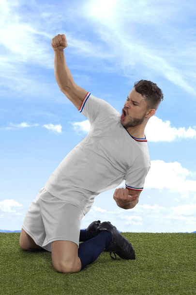 Professional soccer player with a white USA national team jersey shouting with excitement for scoring a goal with an expression of challenge and happiness on field grass and cloud background - Фото, изображение