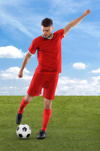 Professional soccer player with red Canada national team jersey about to score a goal with an expression of challenge and decision on his face on field grass and cloud background - Фото, изображение