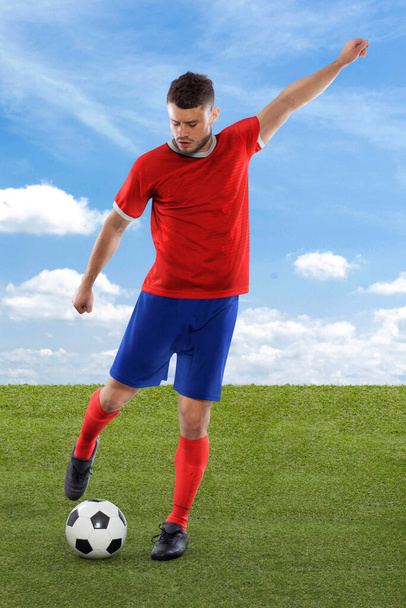 Professional soccer player with red Costa Rica national team jersey about to score a goal with an expression of challenge and decision on his face on field grass and cloud background - Photo, Image