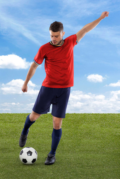 Professional soccer player with red Spain national team jersey about to score a goal with an expression of challenge and decision on his face on field grass and cloud background - Zdjęcie, obraz