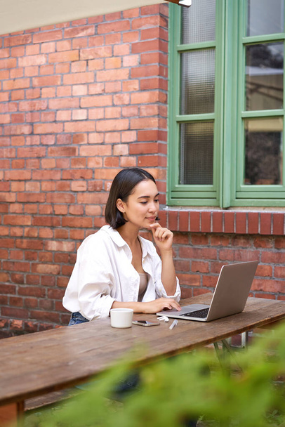 Portré elegáns fiatal nő, barna lány laptop, ül a szabadban, és használja a számítógépet. - Fotó, kép
